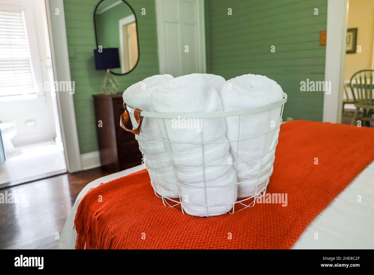 gli asciugamani puliti arrotolati in un cestino di filo seduto su un letto in una camera da letto degli ospiti Foto Stock