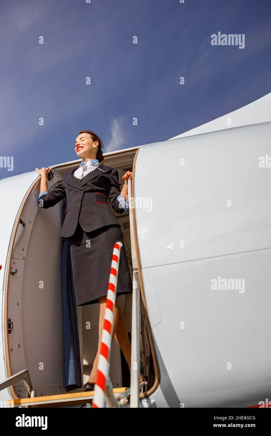 Donna allegra stewardess in piedi nella porta dell'aeroplano Foto Stock