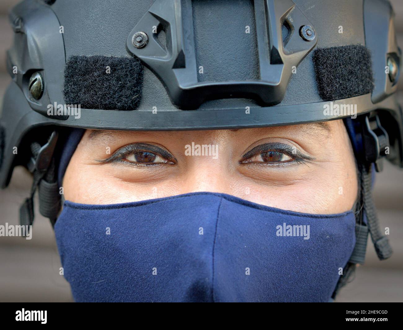 Ufficiale tattico femminile di polizia motociclistica con maschera facciale e casco protettivo guarda con occhi marroni sorridenti e eye-make allo spettatore. Foto Stock