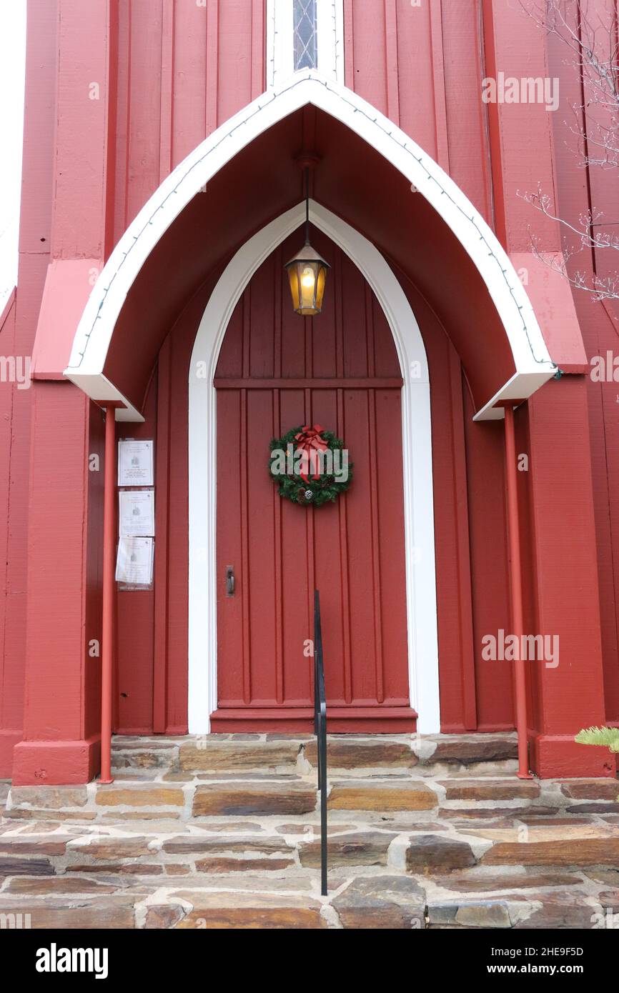 Festa Natale corona su una porta chiesa di legno rosso accoglie la stagione dell'Avvento. Una luce dorata è appesa sulla porta. Foto Stock