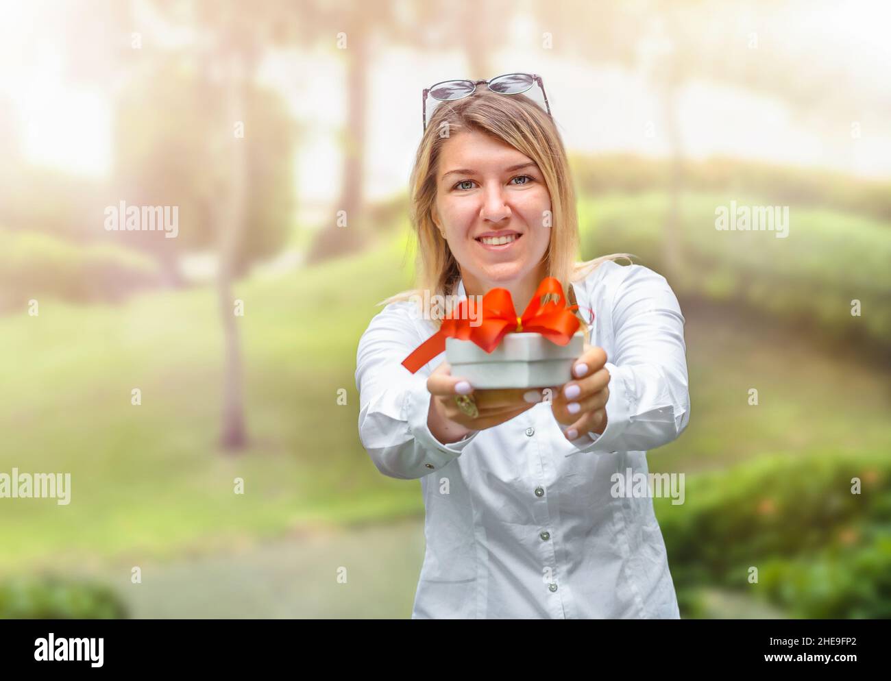 La ragazza tiene fuori la scatola del regalo con il nastro rosso all'aperto Foto Stock