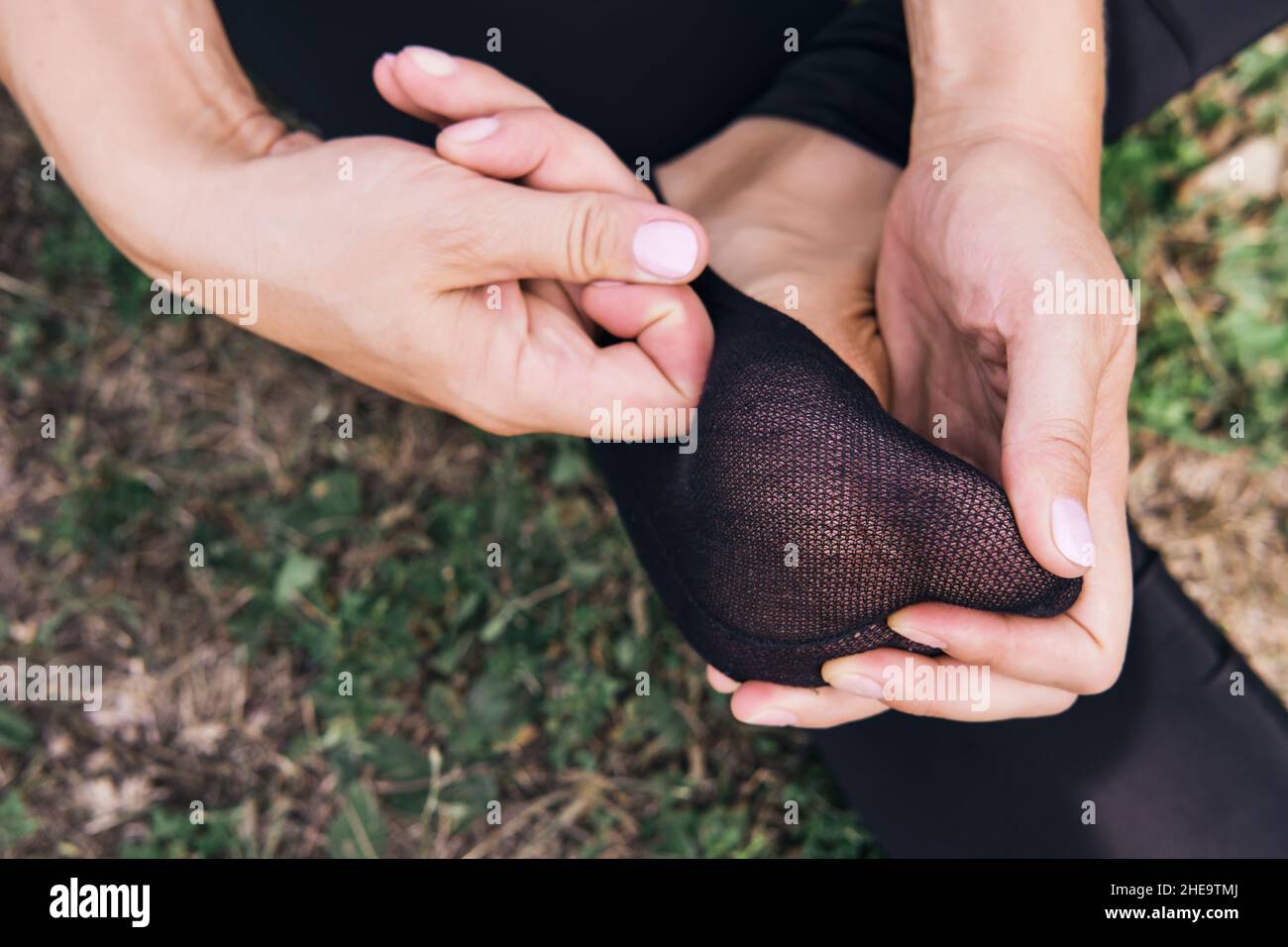 Donna seduta sull'erba e massaggia il piede in calza primo piano. Dolore o crampi nel piede. Foto Stock