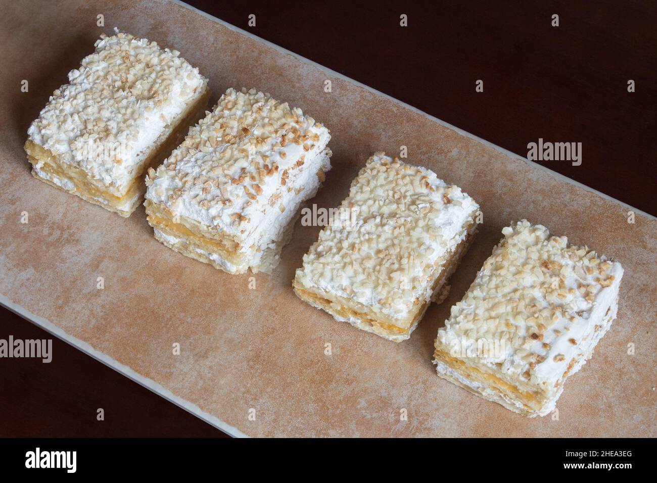 Diverse porzioni individuali di crosta in fila su un vassoio testurizzato astratto, color pastello dolce tradizionale pasta sfoglia dessert con panna. Foto Stock