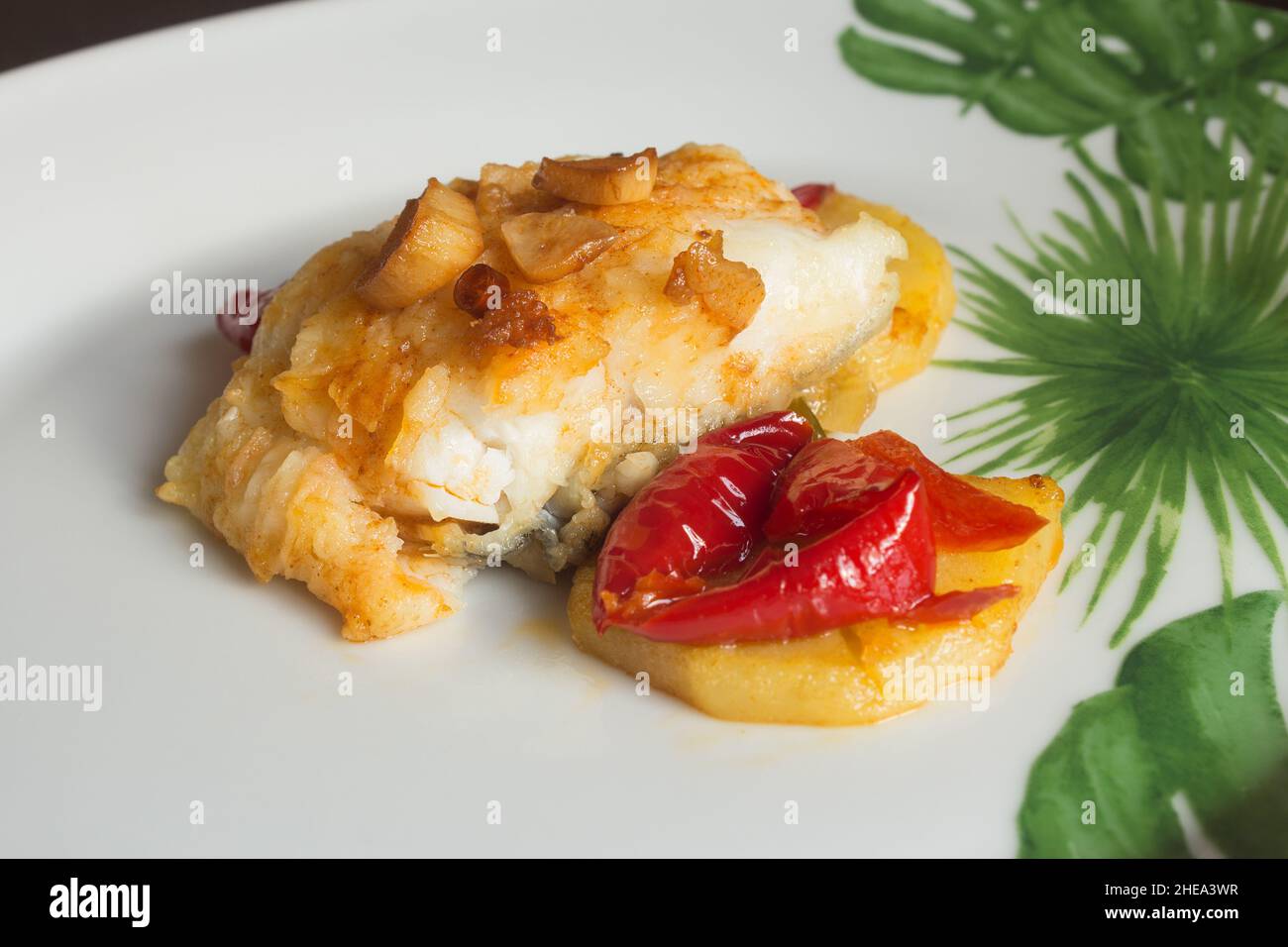 Placcatura di merluzzo verniciato con uovo tostato accompagnato da peperoni rossi, patate e aglio su un piatto con decorazione astratta. Pesce e salute. Foto Stock
