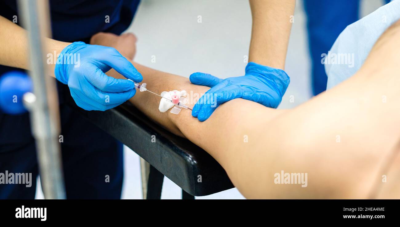 Focalizzazione selettiva sulle mani di un medico che inserisce un ago del catetere in una vena nel braccio del paziente. Le mani del medico con i guanti sterili inserire un ago nella mano della persona per iniettare la soluzione salina. Foto Stock