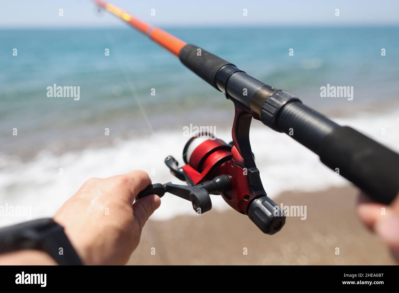 Le mani tengono una canna da pesca sullo sfondo della costa marina Foto Stock