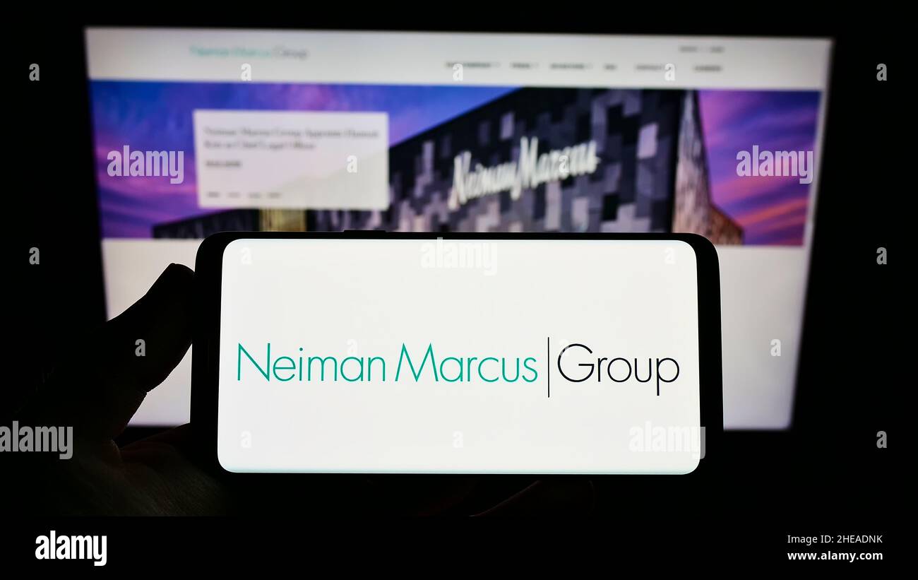 Persona che tiene uno smartphone con il logo della società di vendita al dettaglio statunitense Neiman Marcus Group Inc. Sullo schermo di fronte al sito Web. Mettere a fuoco sul display del telefono. Foto Stock