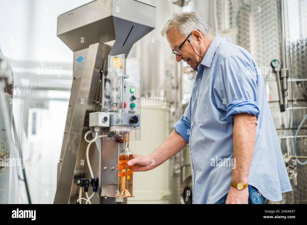 L'uomo anziano usa la macchina per sughero la bottiglia di vino nella sua distilleria. Foto Stock