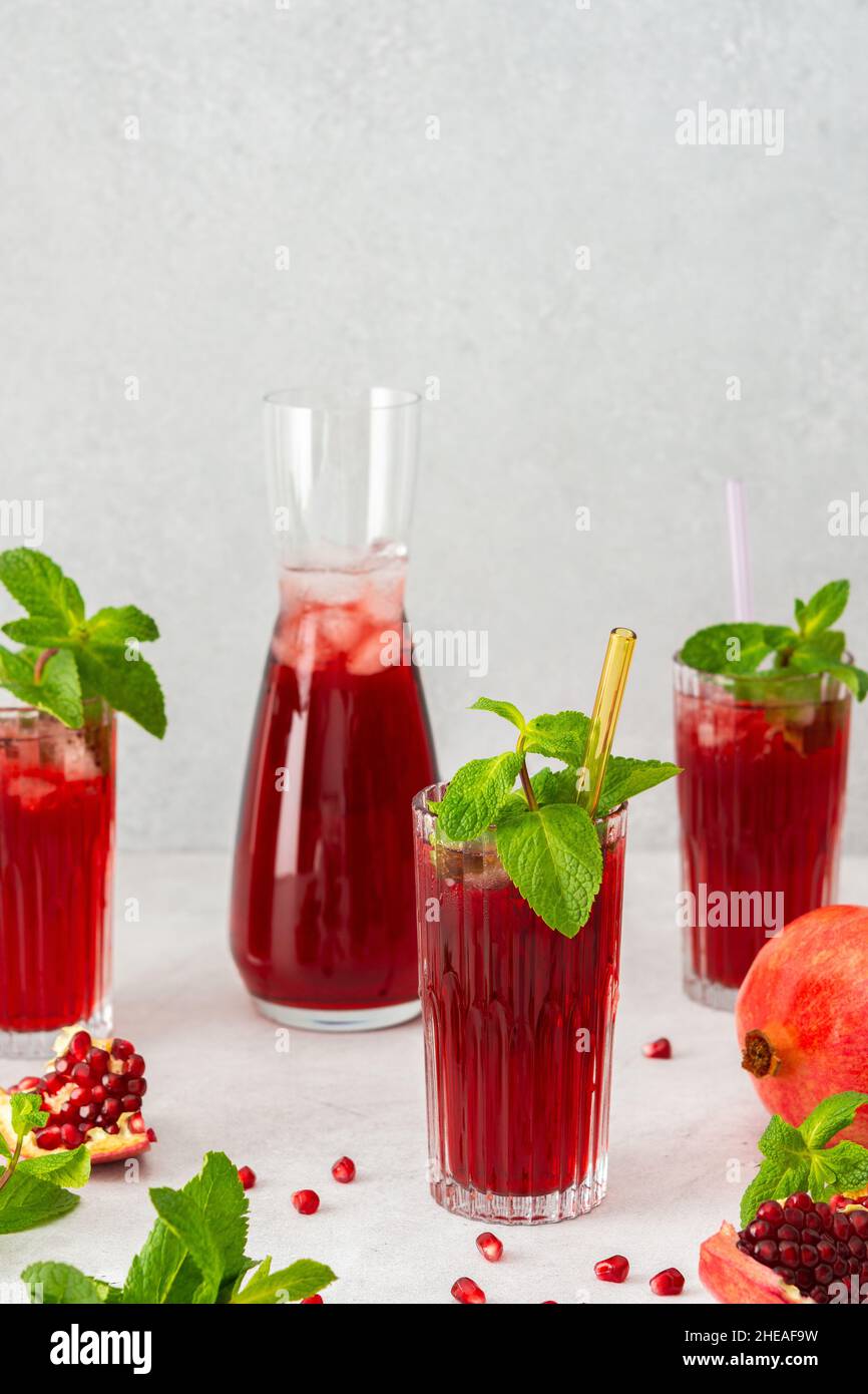 Rinfrescante succo di melograno in bicchieri con paglia di menta e vetro, caraffa di succo di frutta e ghiaccio, bevanda fredda Foto Stock