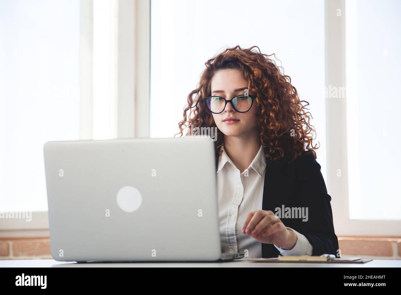 Portret di una giovane donna di successo con capelli rossi ricci in un il  costume da lavoro e gli occhiali funzionano in un ufficio su un computer  portatile Foto stock - Alamy