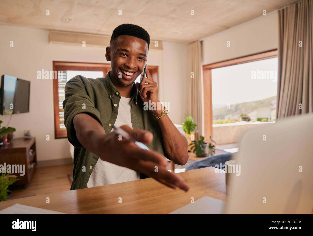 Giovane adulto nero maschio gesturing verso lo schermo del laptop mentre in discussione sopra il telefono. Faccia espressiva. Lavorare in remoto da casa moderna Foto Stock