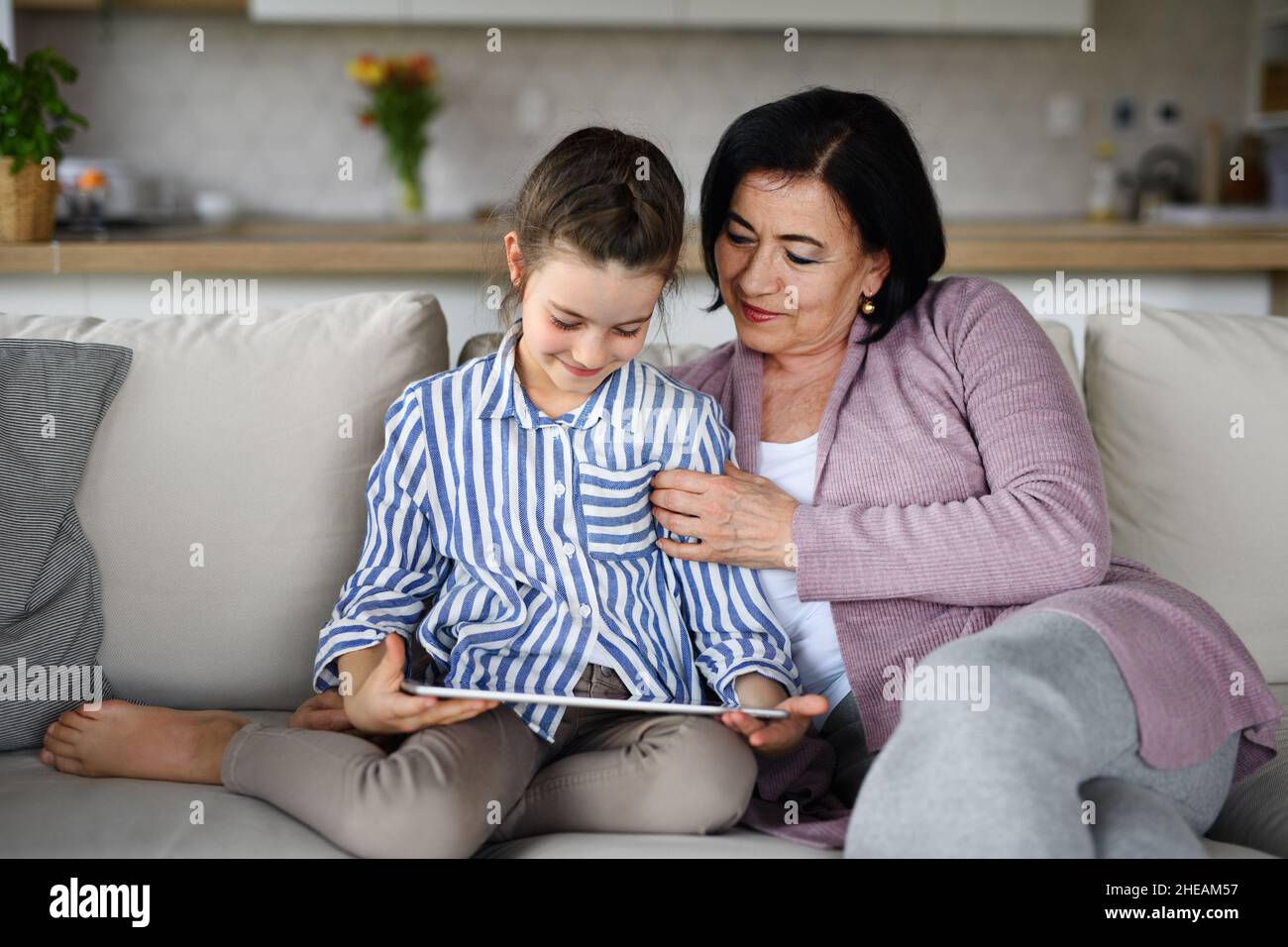 Ragazza piccola felice con nonna in casa, utilizzando tablet. Foto Stock