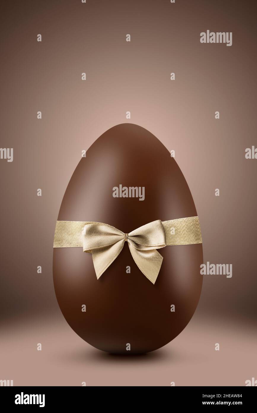Uovo di pasqua al cioccolato con nastro d'oro su sfondo marrone Foto Stock