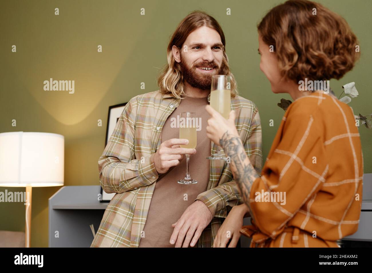 Una giovane coppia sorride e beve champagne durante la conversazione in camera Foto Stock