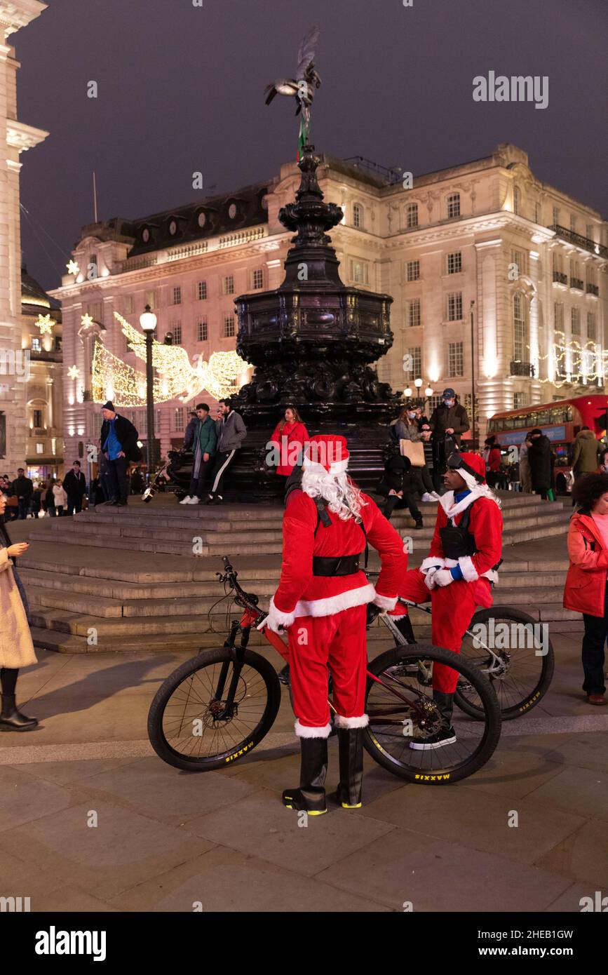 Uomini vestiti con costumi di Santa in bicicletta accanto alla Shaftesbury Memorial Fountain, Piccadilly, Londra Foto Stock