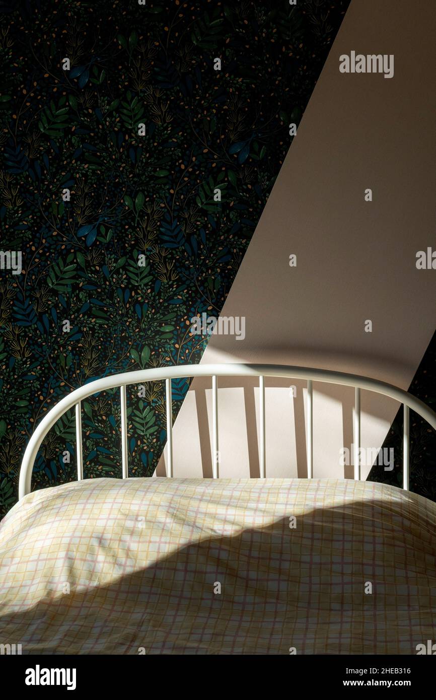 Un intimo angolo camera da letto con luce soffusa che scorre sul letto ben fatto e sulle pareti a motivi geometrici in uno spazio tranquillo Foto Stock