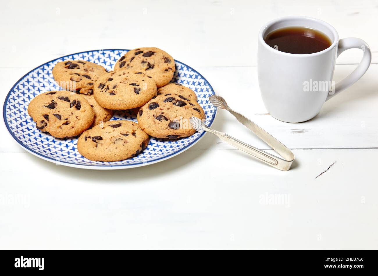 Tazza bianca con caffè e biscotti tradizionali su fondo bianco di legno, primo piano. Gustosa colazione, concetto di routine del mattino Foto Stock