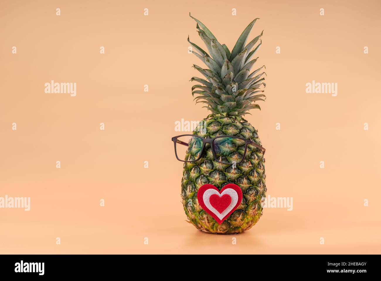 Interpretazione della frutta di ananas nell'immagine umana con i vetri e il concetto di cuore della medicina o degli amanti di giorno di San Valentino. Spazio di copia su sfondo giallo Foto Stock
