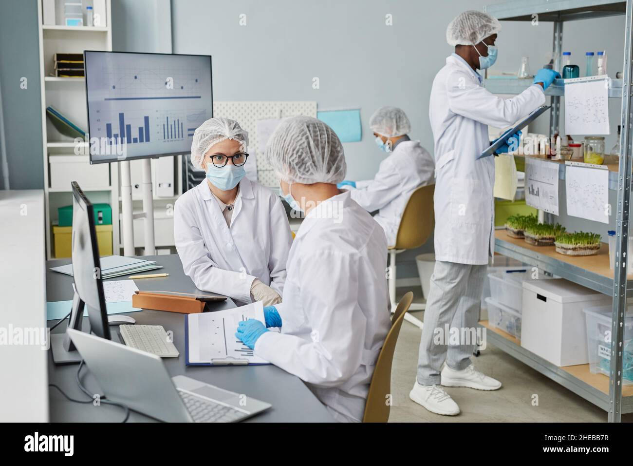 Gruppo di persone in indumenti protettivi che cooperano con documenti e analisi in laboratorio Foto Stock