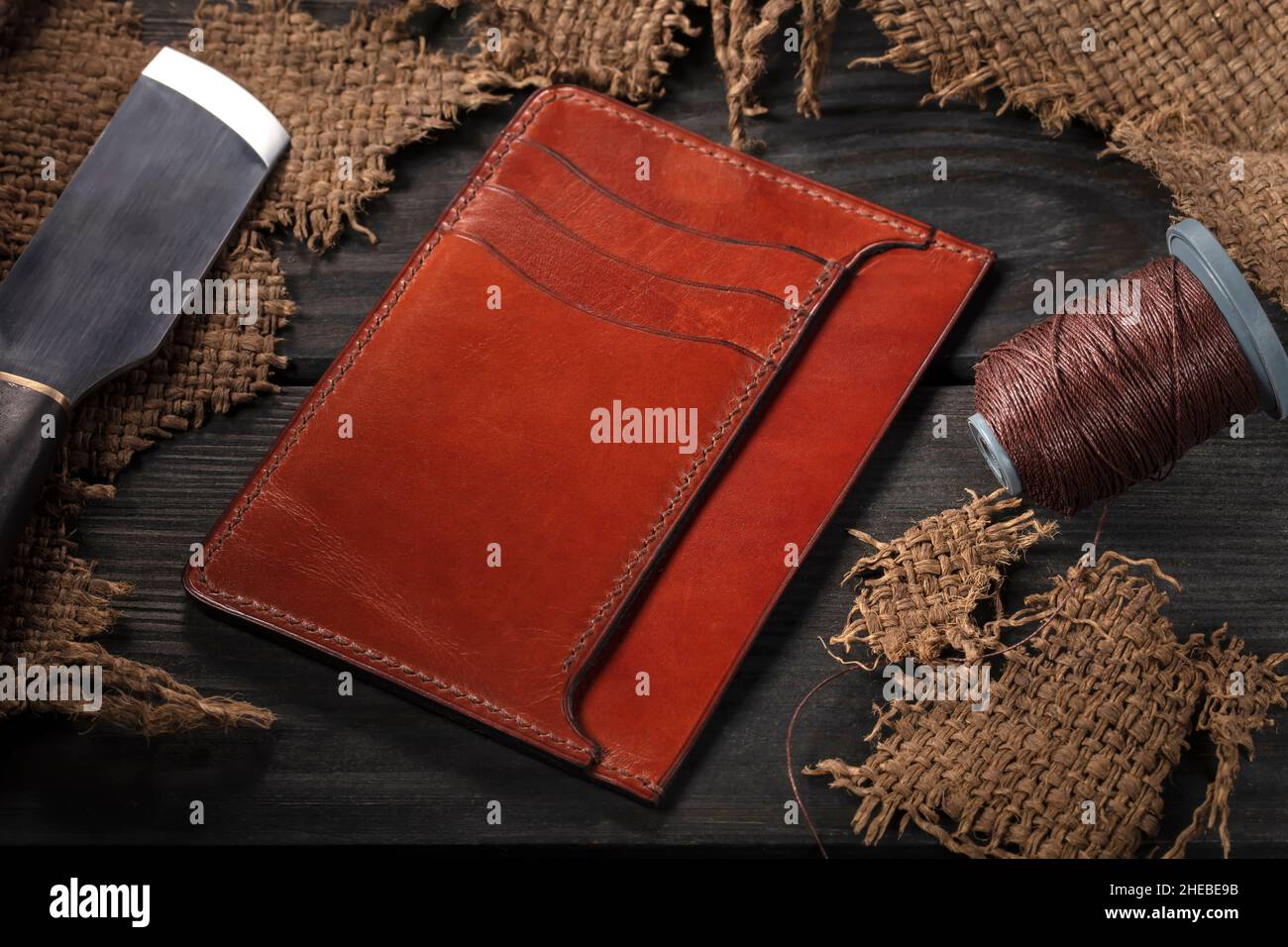 Realizzazione di portafogli in pelle. Su un tavolo di legno c'è un  portafoglio in pelle, un rocchetto di filo e un coltello Foto stock - Alamy