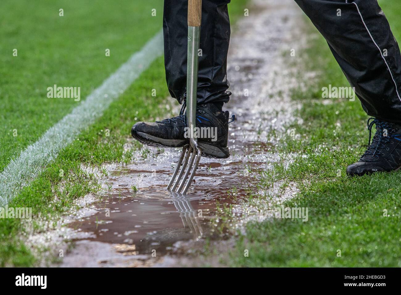 Membro del personale di terra che pratica l'aerazione dell'erba per scaricare l'acqua dal campo da calcio con acqua Foto Stock