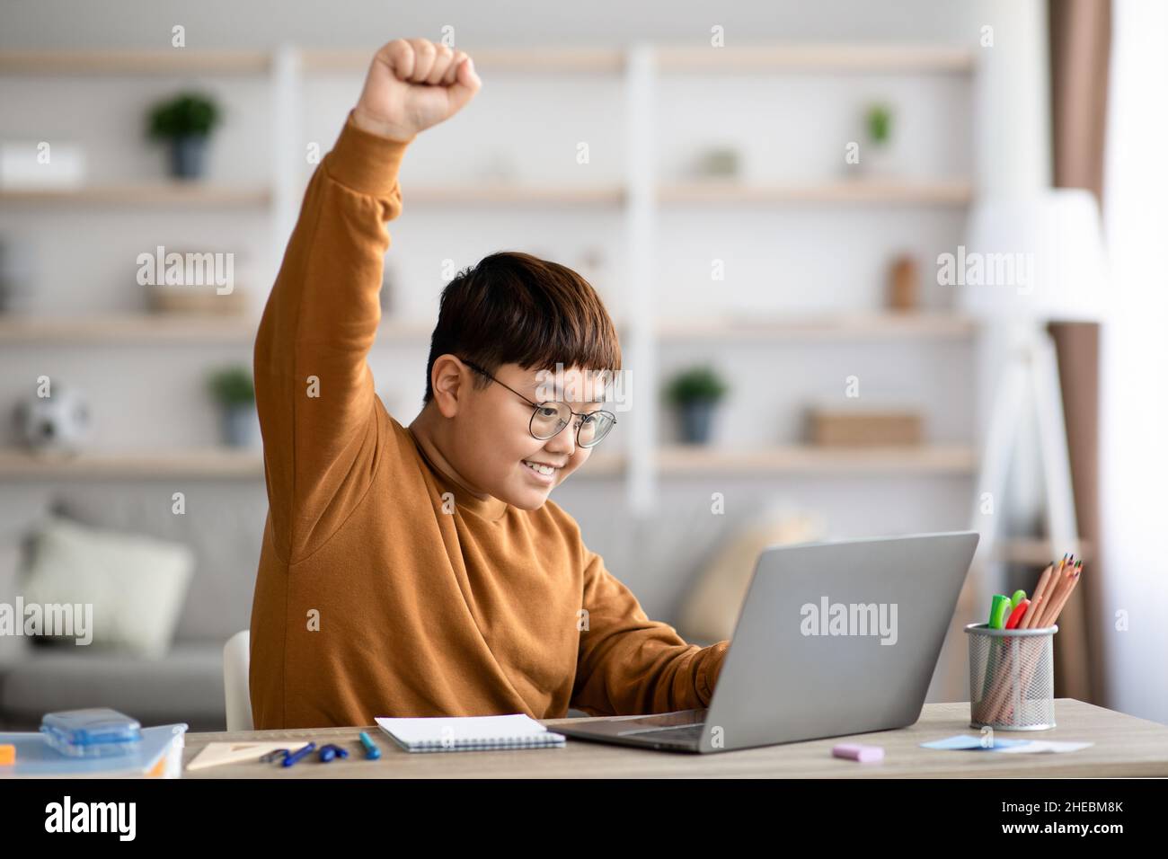 Gioioso adolescente cinese che usa il laptop, alzando la mano Foto Stock
