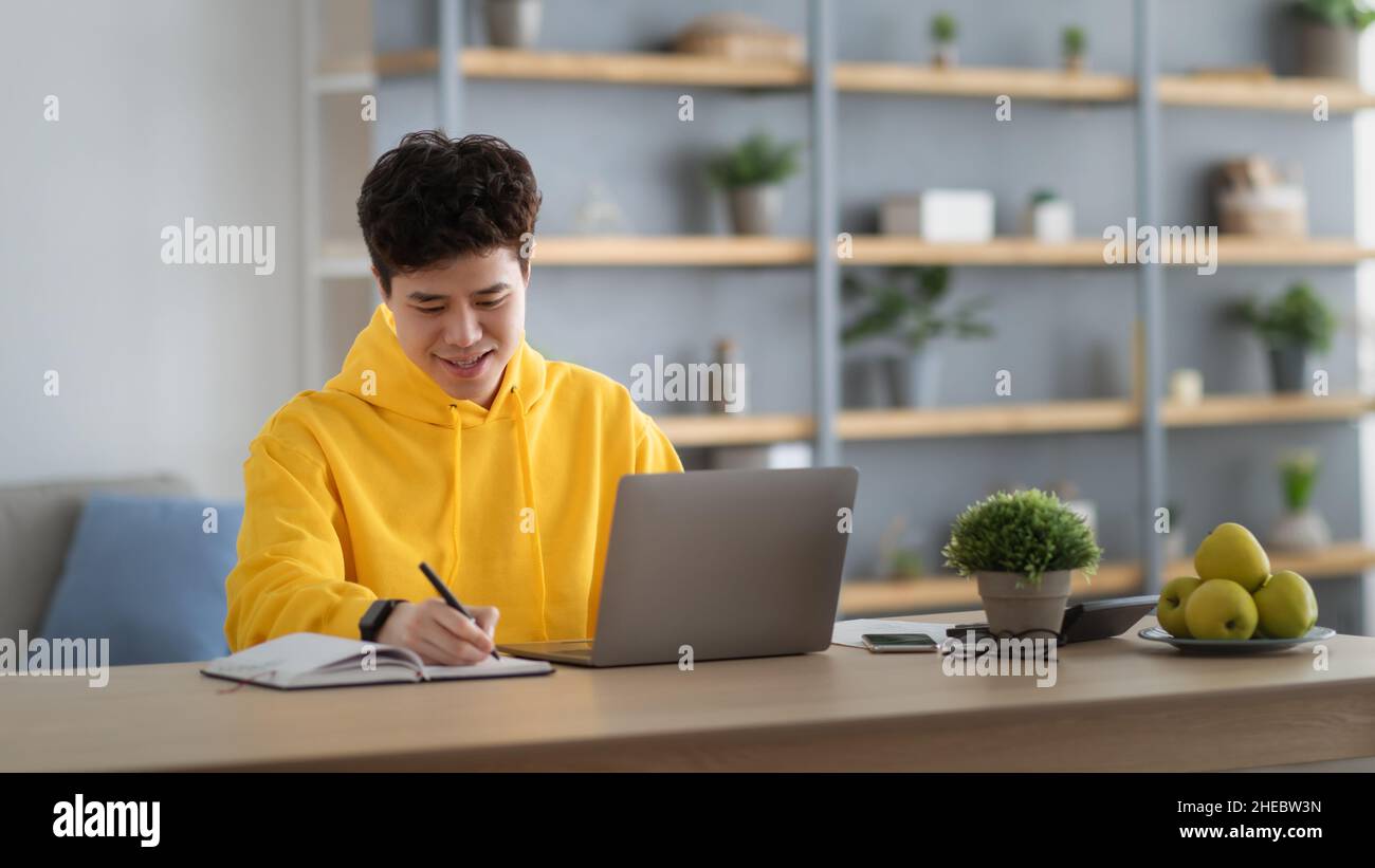 Uomo asiatico sorridente che lavora su un computer portatile e scrive Foto Stock