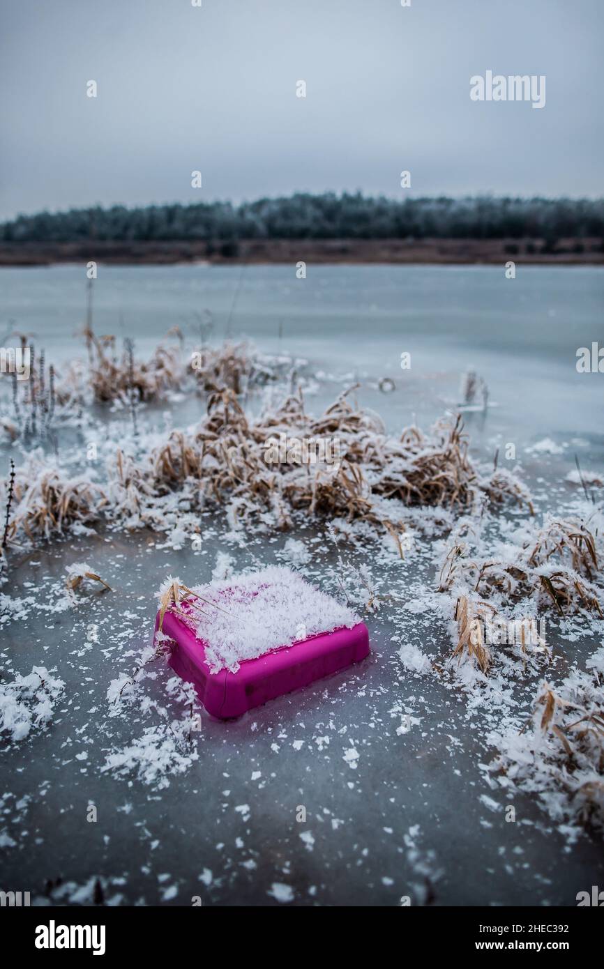 Rifiuti di plastica in acqua congelata, pezzo di plastica rosa coperto di neve parzialmente congelato in ghiaccio, rifiuti nel lago, inquinamento ambientale, sito di discarica selvaggia Foto Stock