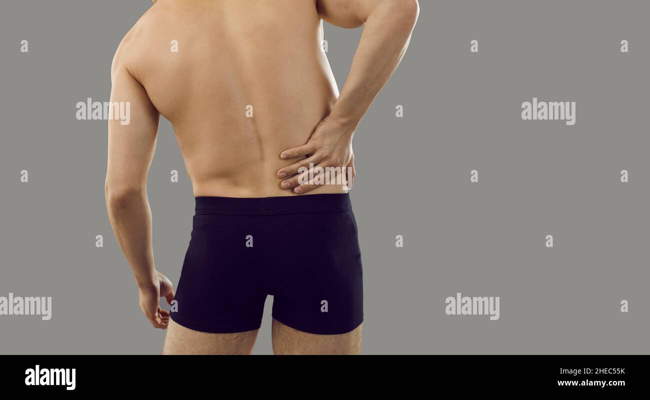 Vista posteriore del giovane uomo che soffre di dolore nella sua parte destra e che tocca la sua parte inferiore della schiena Foto Stock