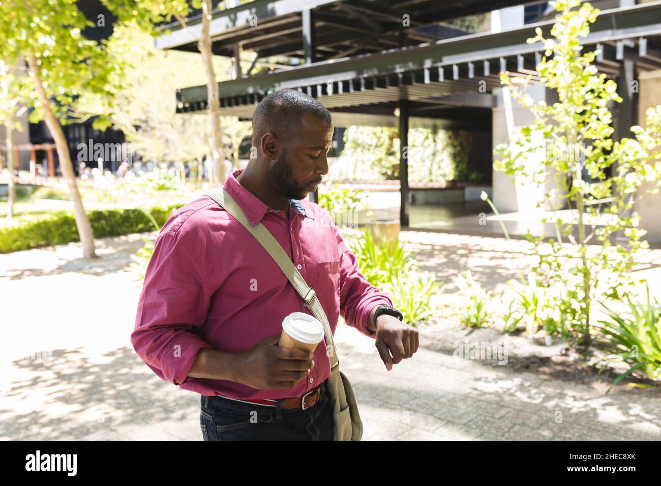 Un uomo d'affari afro-americano che tiene un caffè e usa lo smartwatch mentre è in ufficio Foto Stock