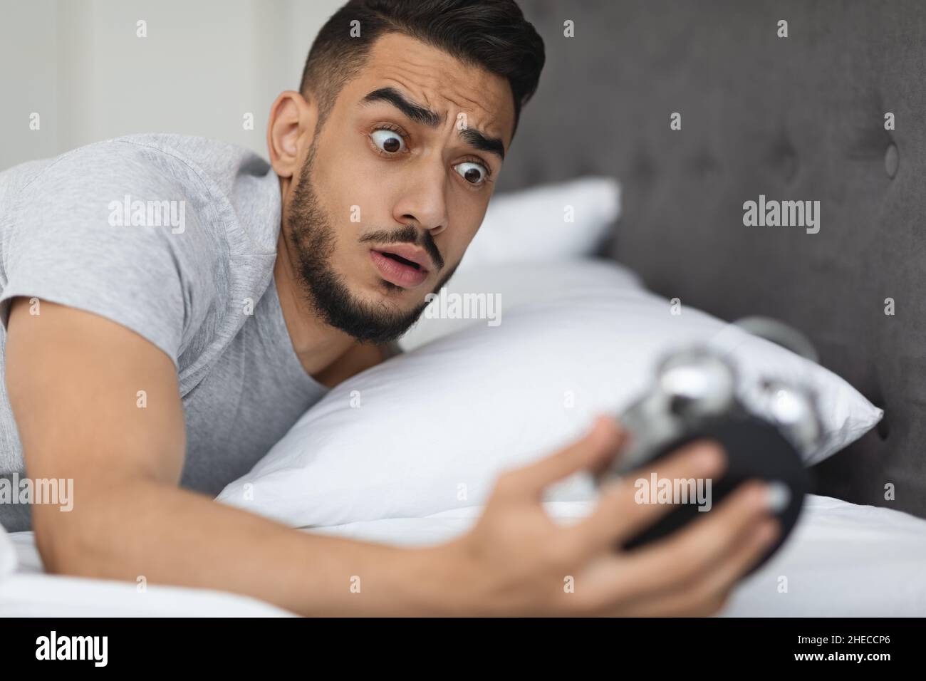 Tardi per lavorare. Shocked ha dormito in Medio Oriente Guy guardando sveglia orologio Foto Stock