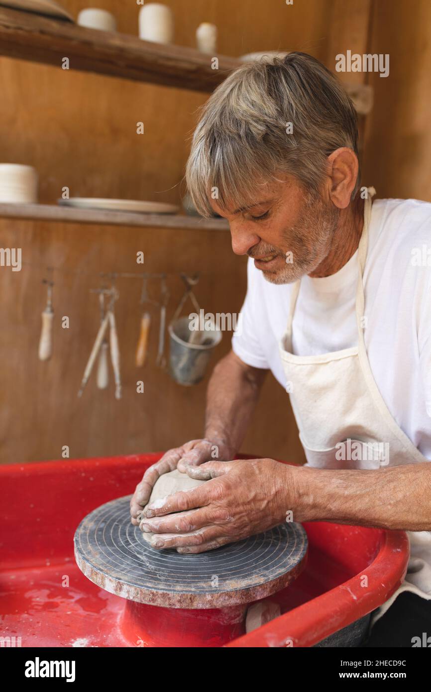 Caucasico maturo ceramista maschio che forma argilla su ceramica ruota in officina Foto Stock