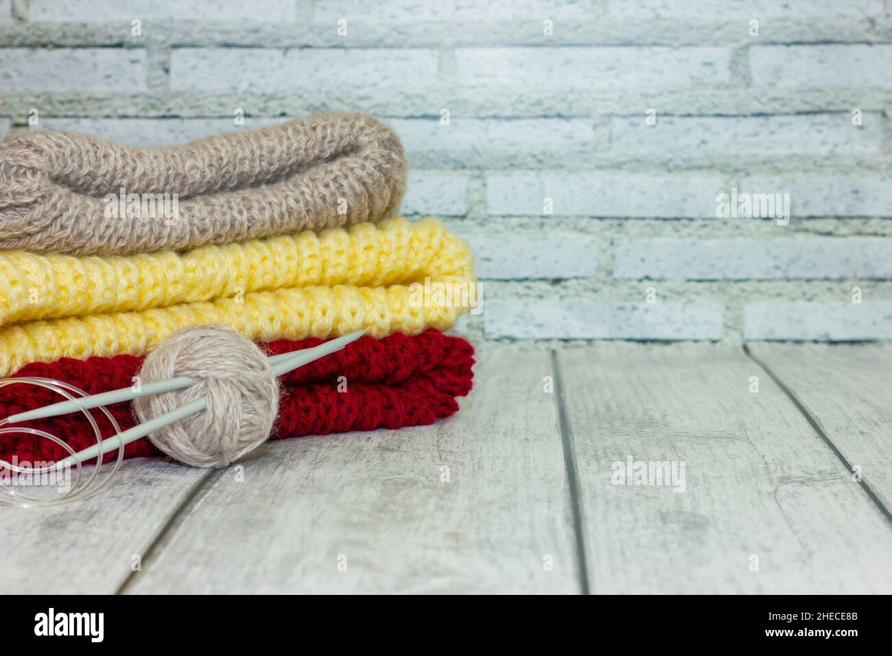 maglie multicolore ripiegate con una sfera di filo e aghi in maglia su sfondo di legno chiaro. concetto artigianale, vendita Foto Stock