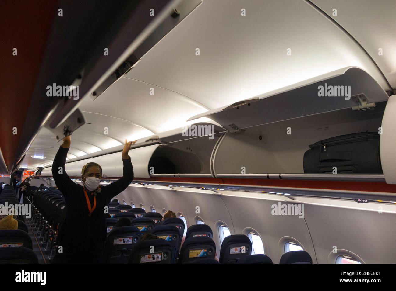 Membro dell'equipaggio di cabina che chiude le porte su armadietto passeggeri a soffitto / armadietti / compartimento / compartimenti per stivare passeggeri borse bagagli di cabina, su un aereo Easyjet Airbus A320 o A319. (128) Foto Stock