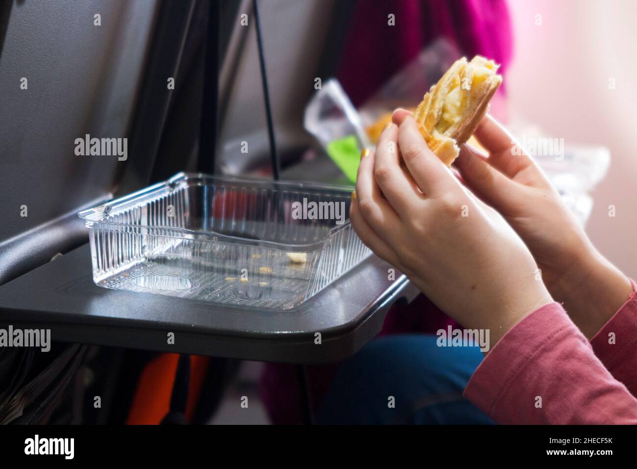 Bambino di nove anni / bambino / ragazza morde in un formaggio e cipolla pastosa che sta mangiando; pasties / ripieno di cibo con molta energia per i bambini, su un tavolo con vassoio sedile, su un Airbus a 320 o un 319 aereo / aereo / aereo. Parte di un pranzo al sacco per lei preparato da un passeggero genitore che ha preso snack alimentari a bordo del volo EasyJet per parte di un pasto self-catering. (128) Foto Stock