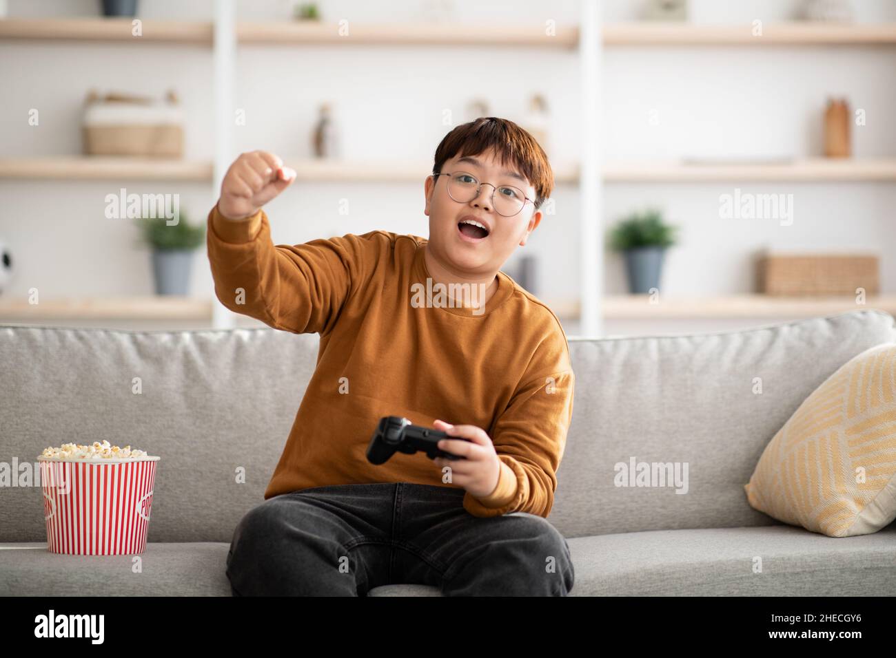 Ragazzo asiatico emozionale che gioca a casa il videogioco portatile Foto Stock