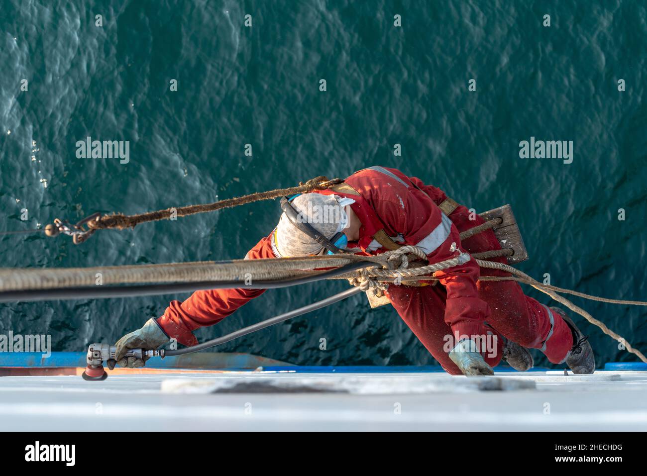 Equipaggio di marinai che lavora in altura e si allontani per preparare la nave per la verniciatura. Manutenzione dell'imbarcazione. Foto Stock