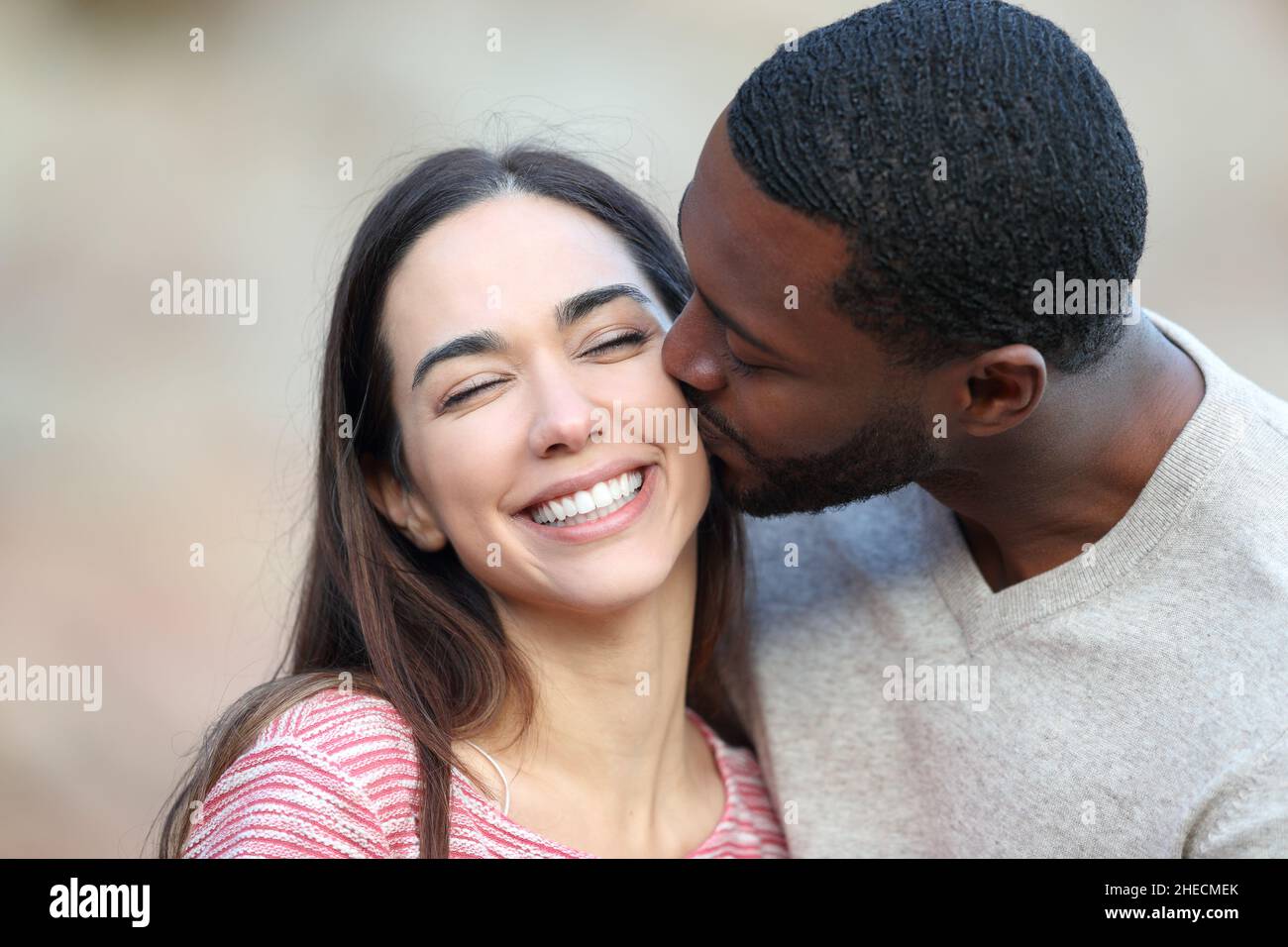 Uomo felice con pelle nera baciare sulla guancia una donna di bellezza all'aperto Foto Stock