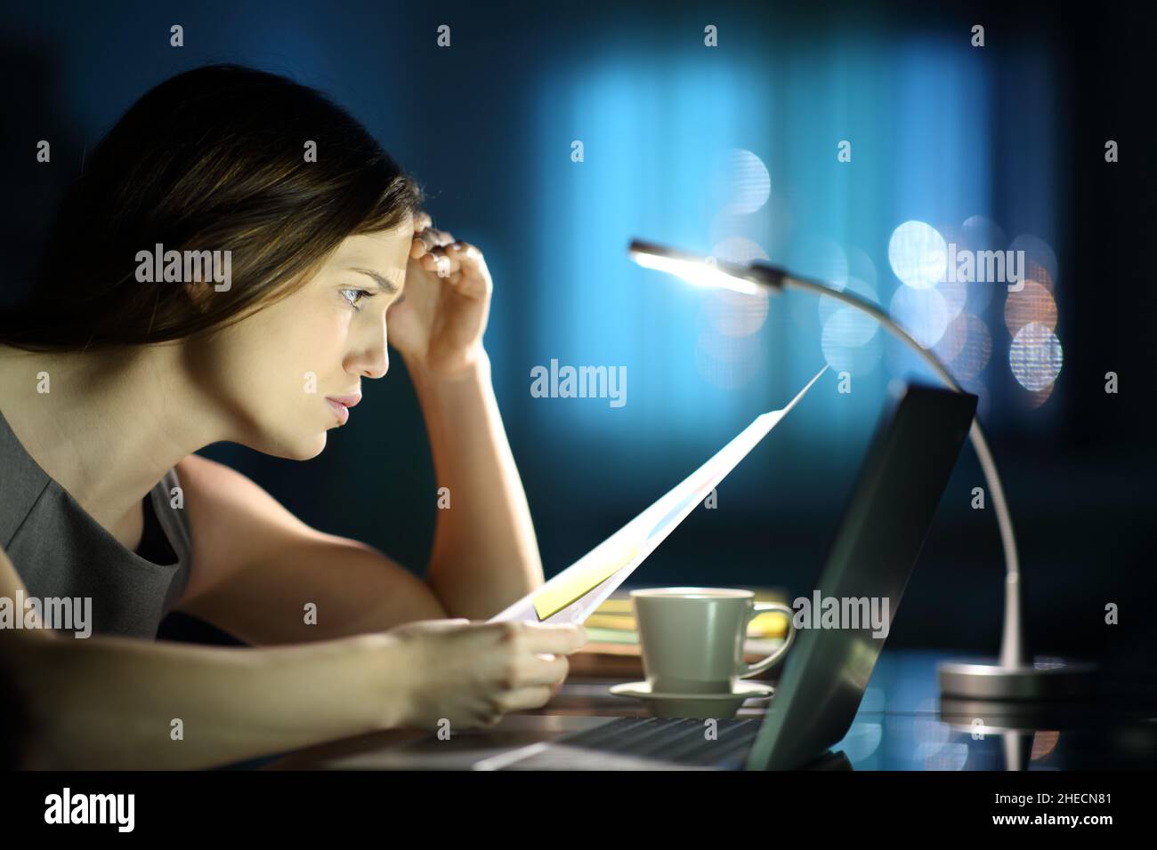 Ritratto laterale di una donna d'affari preoccupata che controlla il documento in linea con un laptop nella notte Foto Stock