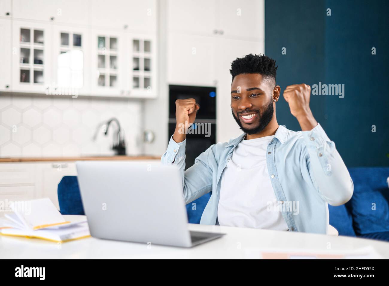 Grande opportunità di lavoro. Ragazzo eccitato che guarda lo schermo del laptop e urla di gioia, ha ricevuto la posta, buone notizie, uomo africano che celebra la vittoria o ha ottenuto un lavoro, sollevando i pugni seduti alla scrivania a casa Foto Stock