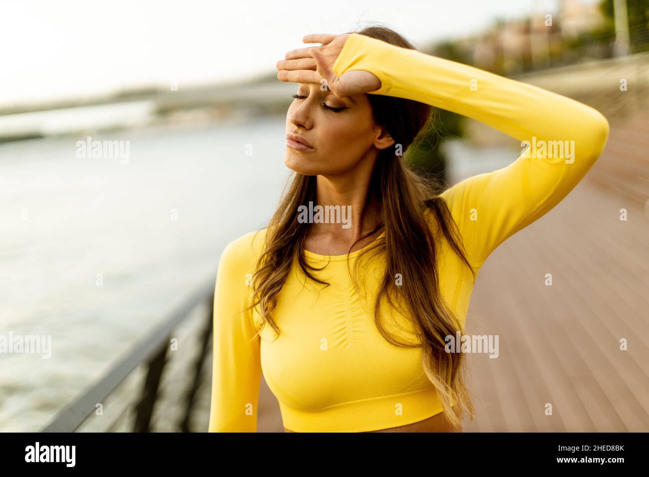 Bella giovane donna che fa una pausa durante l'esercizio sul molo sul fiume Foto Stock