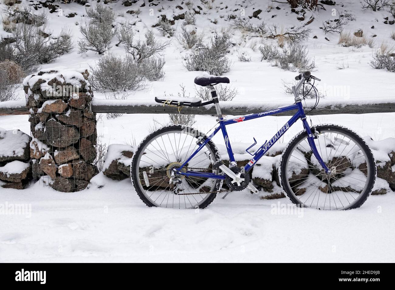 Una vecchia mountain bike si appoggia contro una barriera di legno dopo una neve d'inverno. Foto Stock