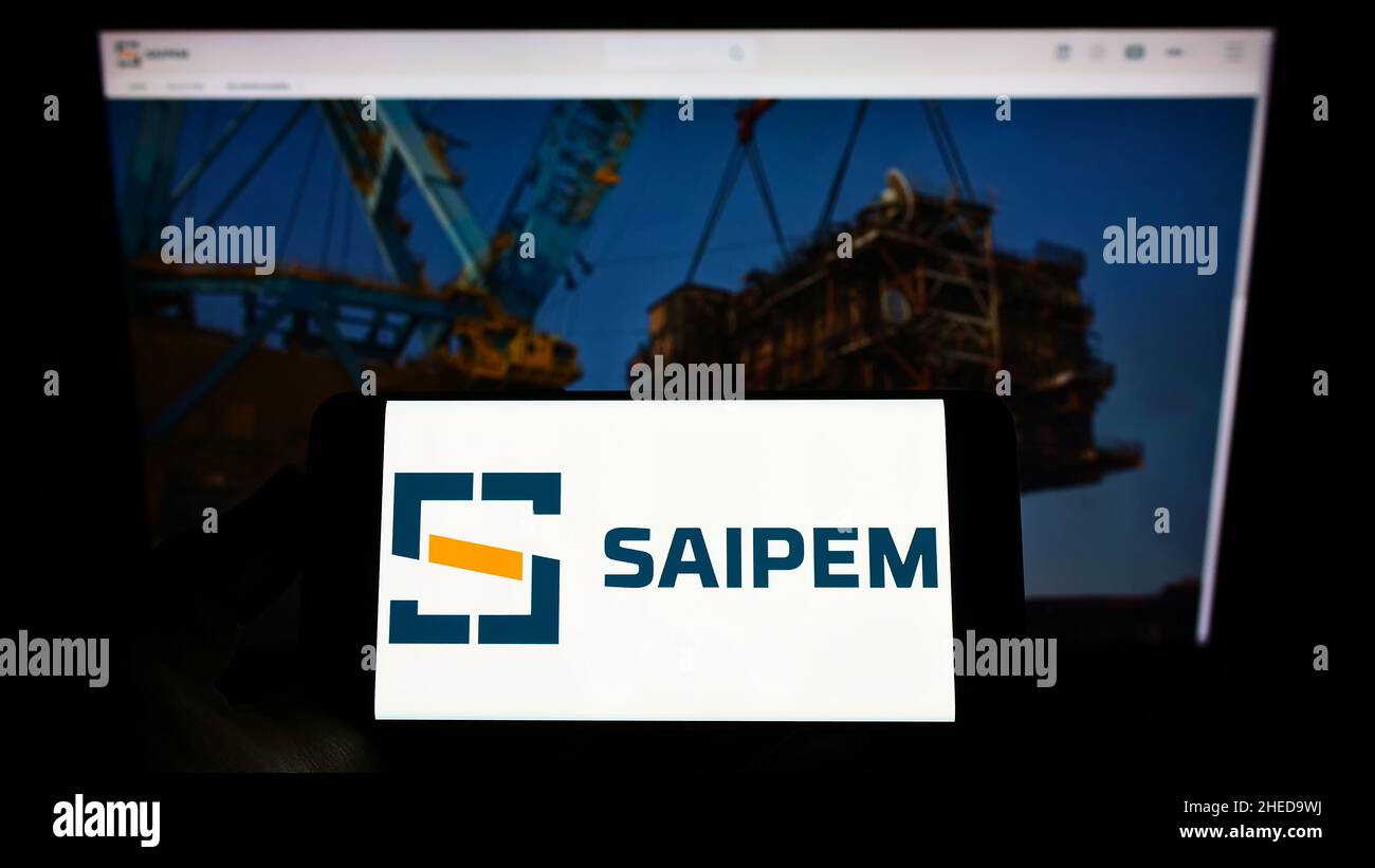 Persona che detiene il cellulare con il logo della società italiana Saipem S.p.A. di servizi petroliferi sullo schermo di fronte alla pagina web. Mettere a fuoco sul display del telefono. Foto Stock