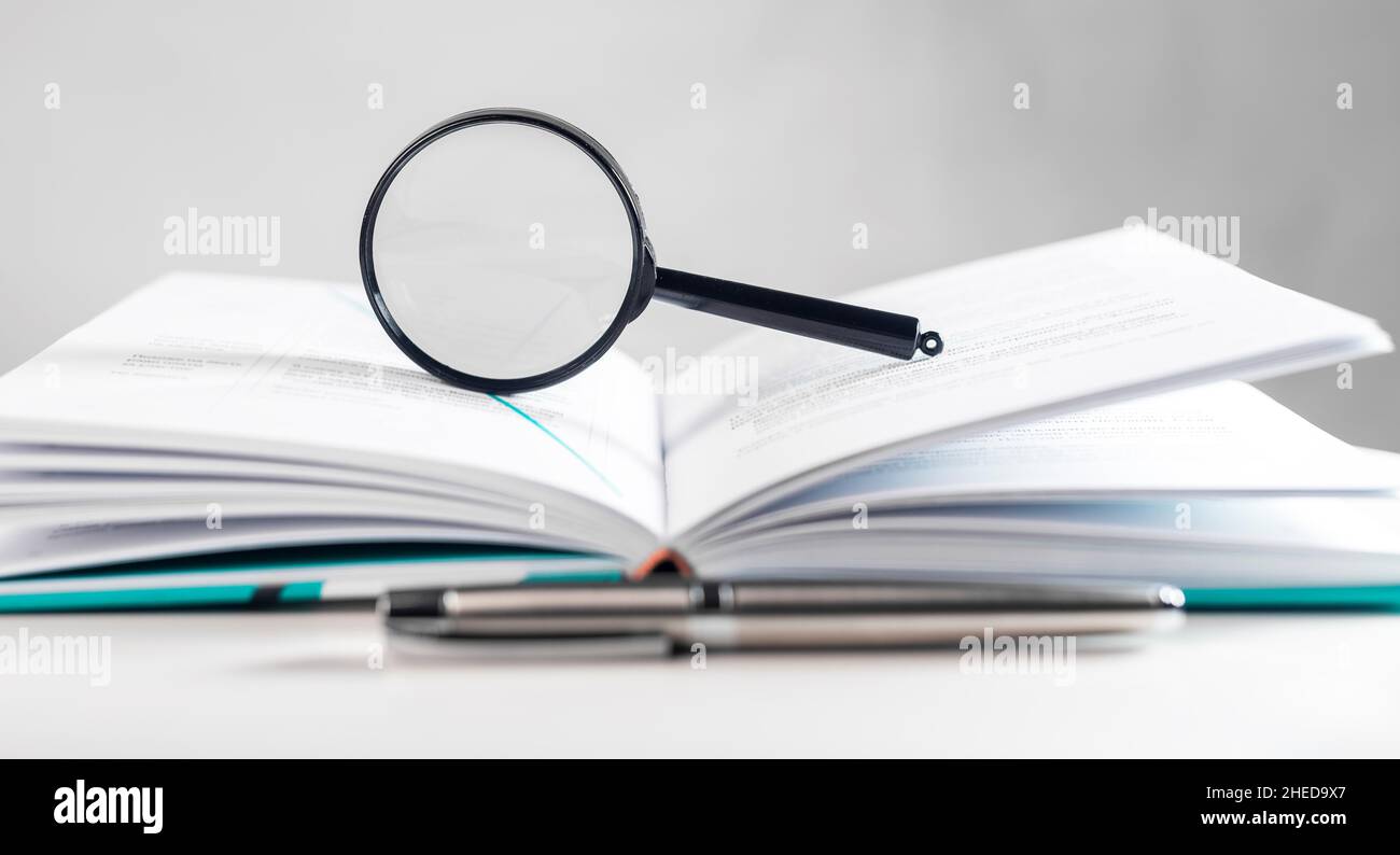 Lente d'ingrandimento sopra il libro di carta aperto con le pagine. Concetto di ricerca accademica. Foto Stock