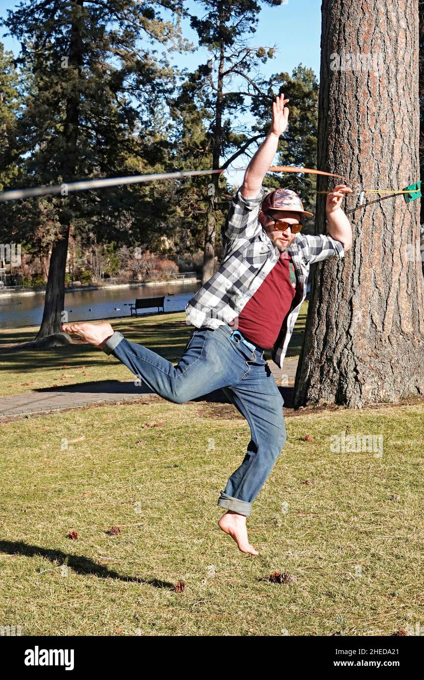 Uno studente universitario pratica un'attività conosciuta come slack Fodera, a piedi una stretta cinghia di nylon. In un parco cittadino di Bend, Oregon. Foto Stock