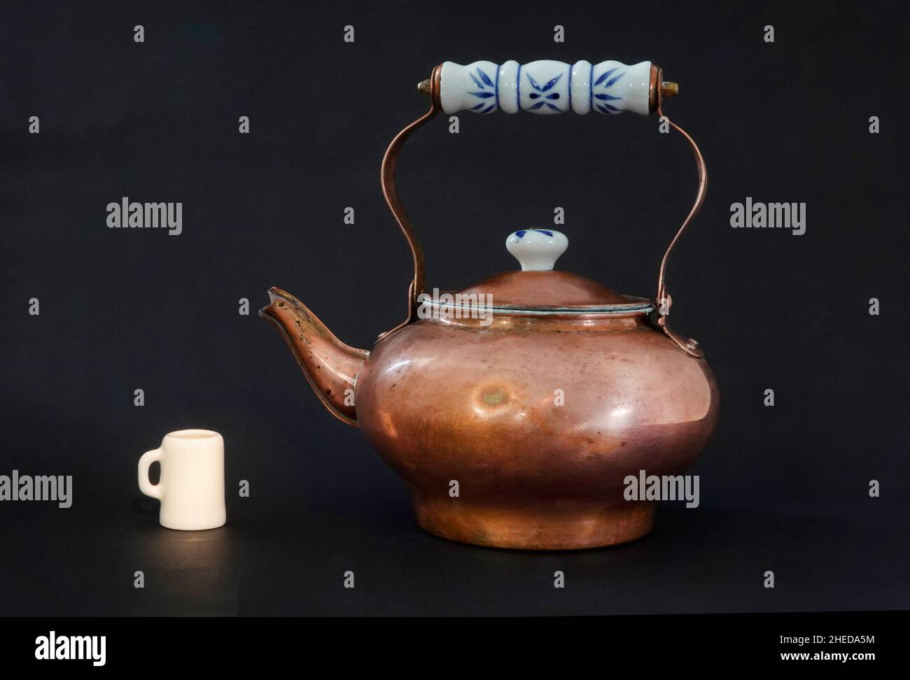 Teiera in rame antico o vintage, con una tazza di porcelano, davanti a uno sfondo nero. Foto Stock