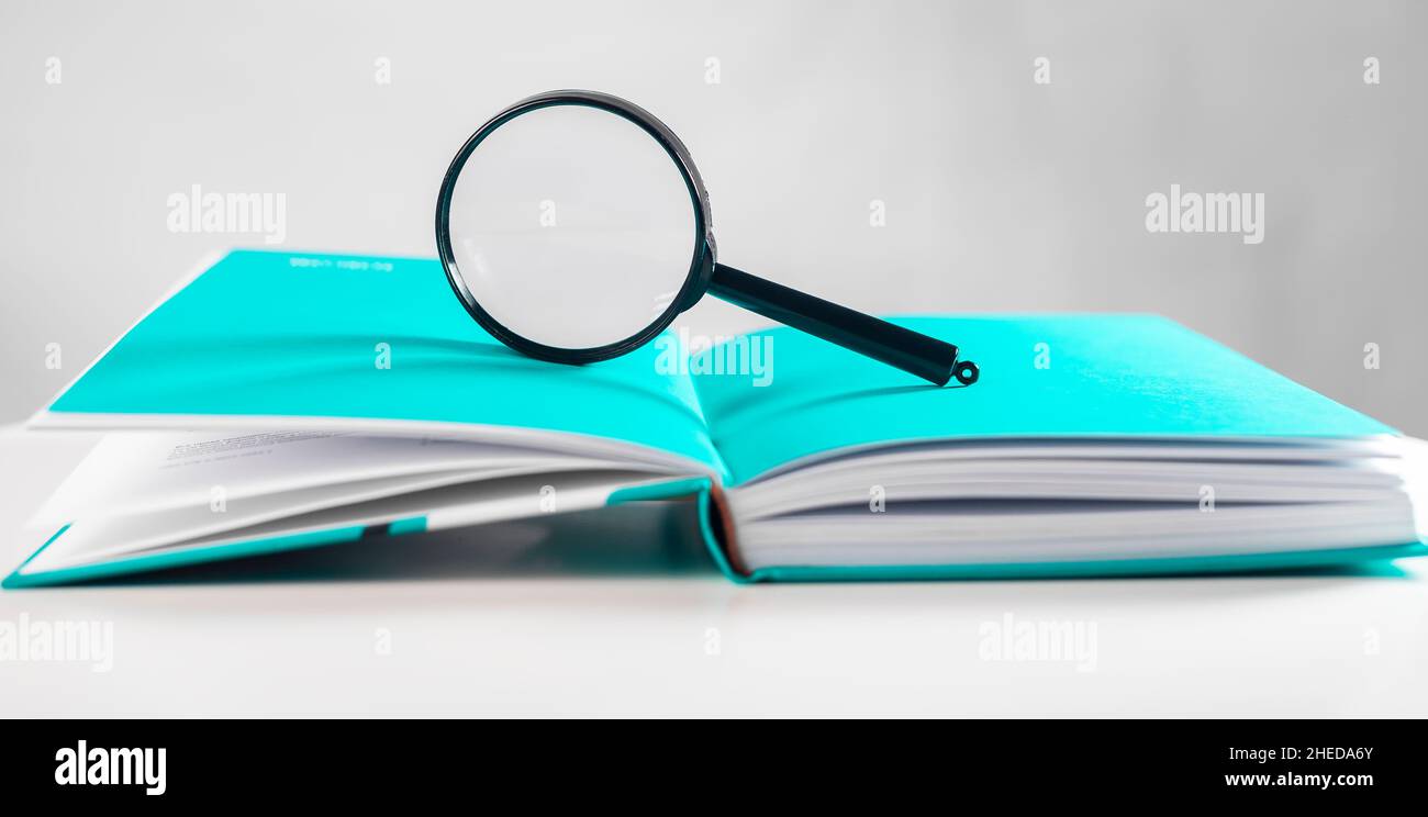 Lente di ingrandimento sopra il libro di carta luminoso aperto. Concetto di conoscenza. Foto Stock
