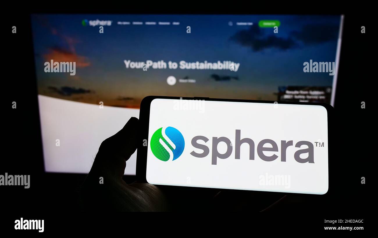 Persona che detiene il cellpohone con il logo della società di software statunitense Sphera Solutions Inc. Sullo schermo di fronte alla pagina web aziendale. Mettere a fuoco sul display del telefono. Foto Stock