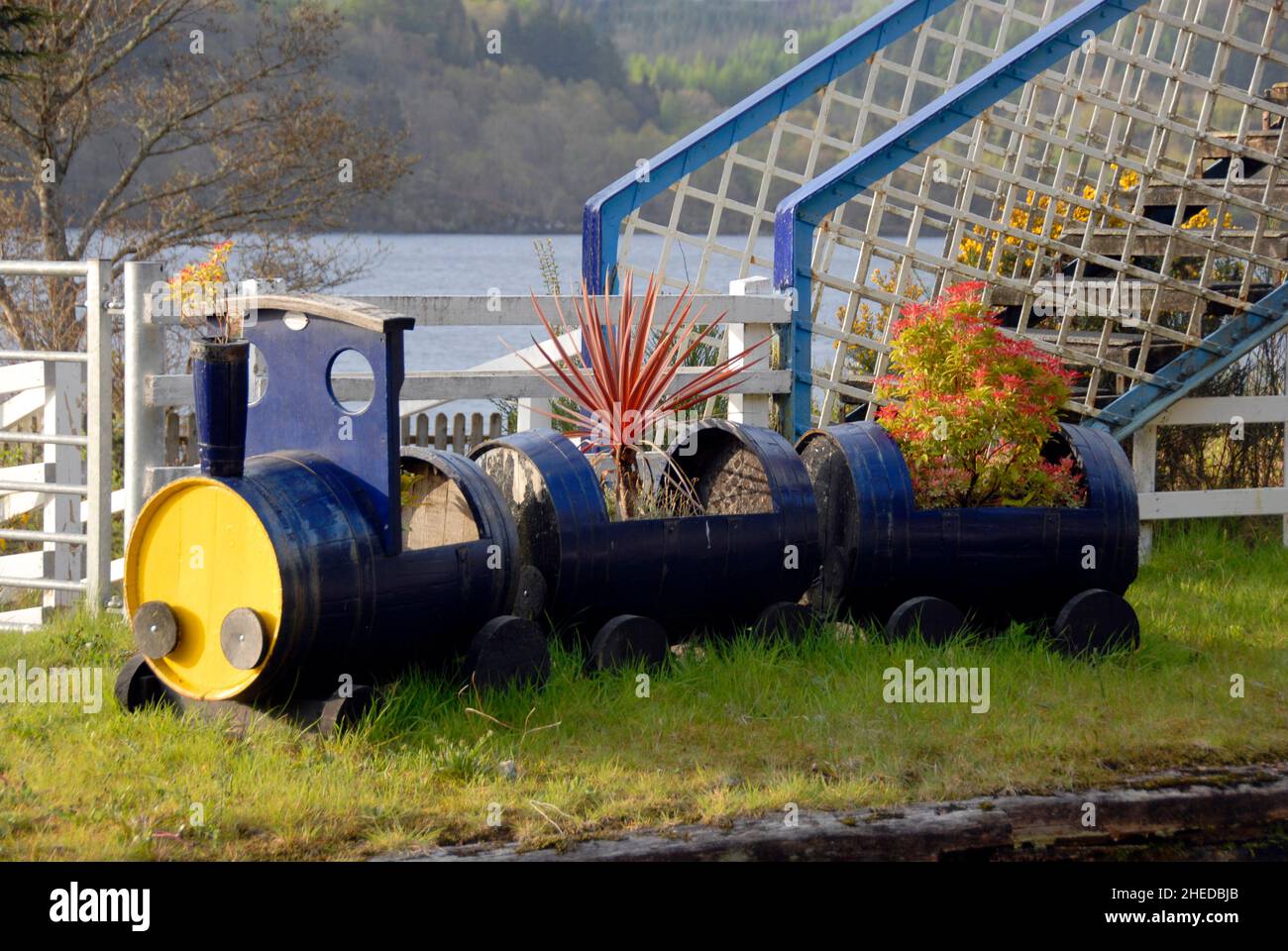Treno ferroviario modello, fatto da vecchi tamburi e riempito di piante, su una piattaforma disutilizzata alla stazione ferroviaria di Loch awe, Loch awe, Scozia Foto Stock