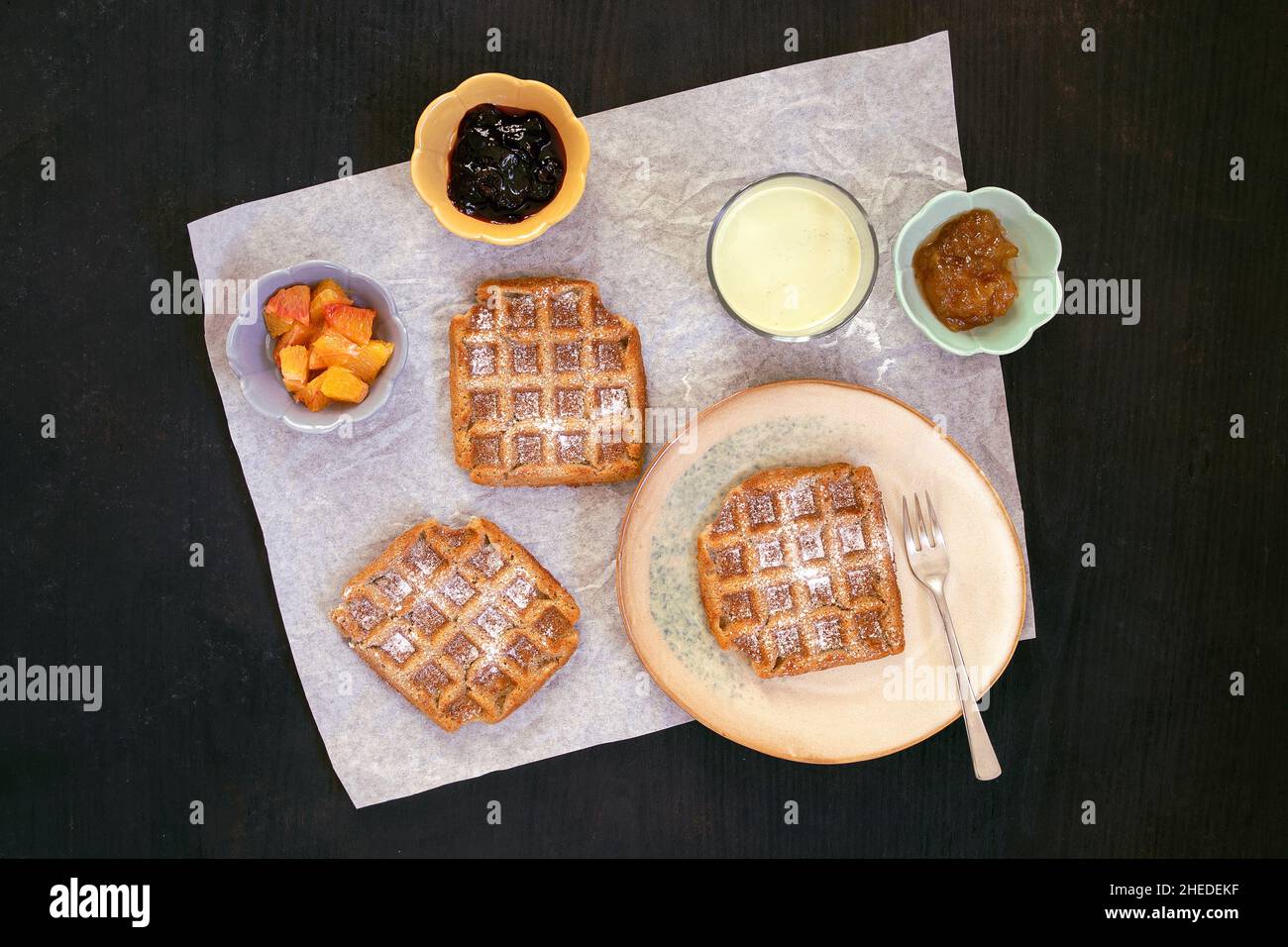 Vista dall'alto di vegan, cialde senza glutine con guarnizioni di marmellata e frutta e sfondo nero di zucchero in polvere. Sana e gustosa colazione fatta in casa. Foto Stock